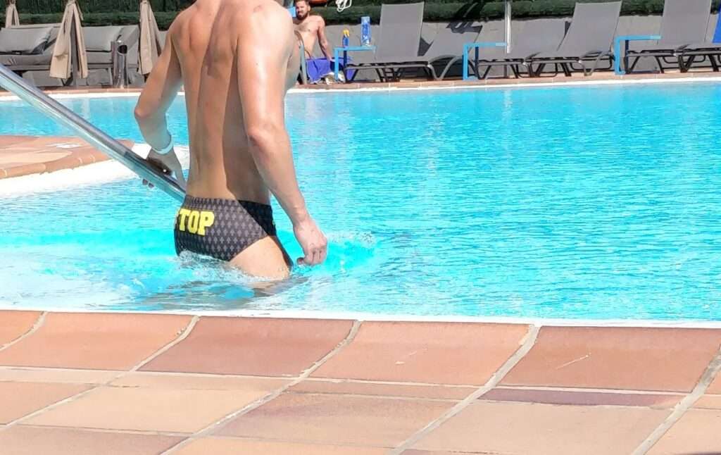 a man in speedo facing away with the word "top" across his bum.