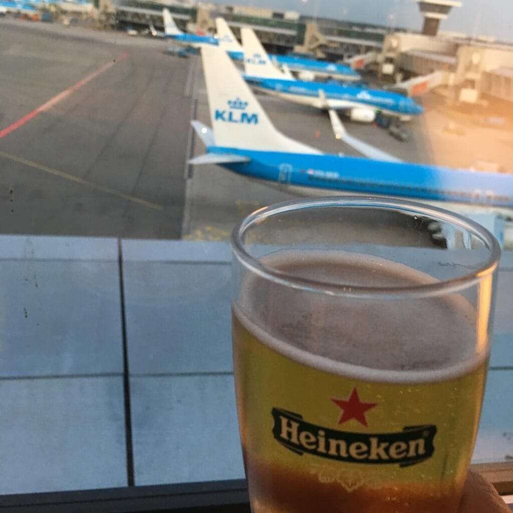 Amsterdam Airport Schiphol view of six KLM planes with blue bodies and white tail fins seen from the lounge at Schiphol with a glass of Heineken in the foreground.