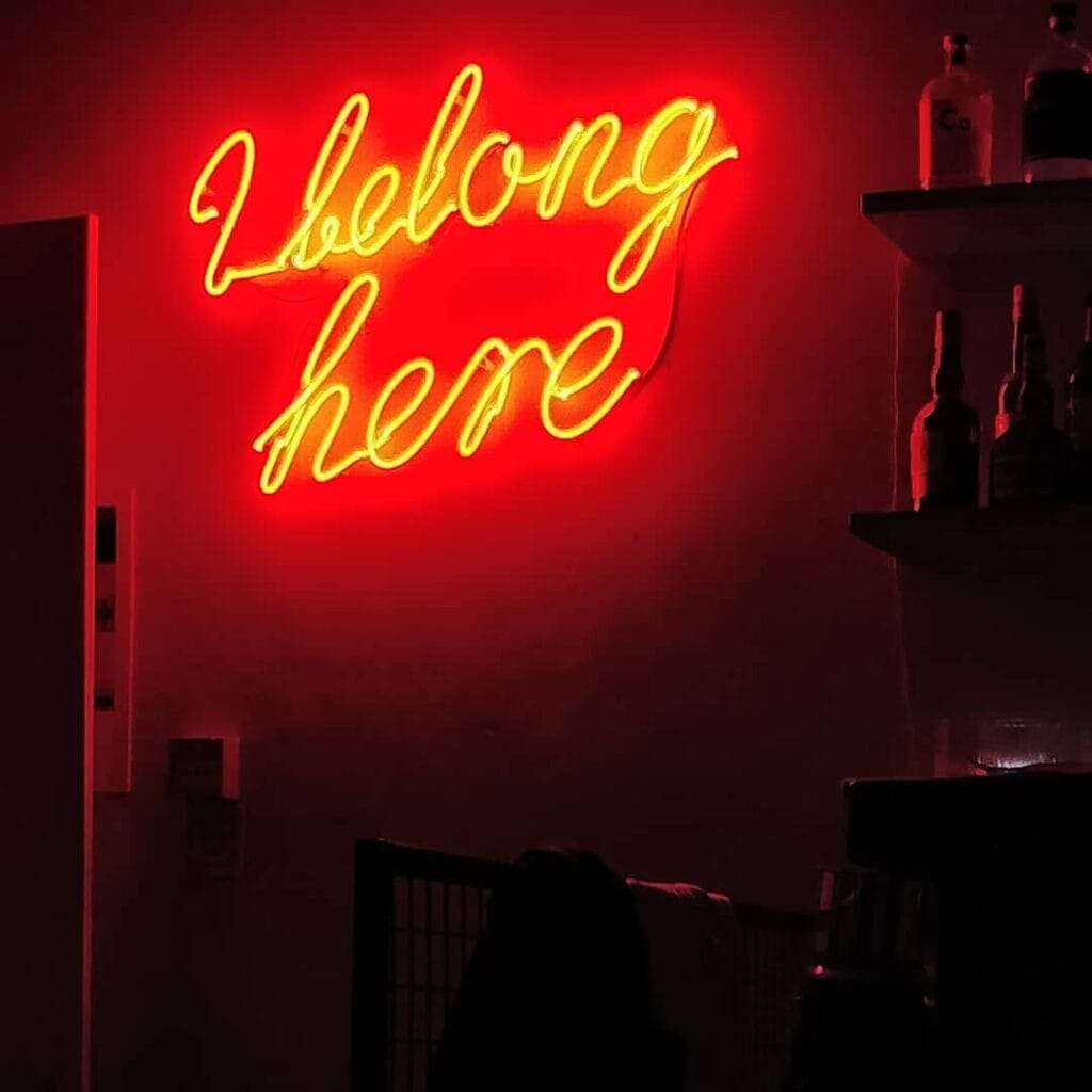 A red neon sign that reads "I belong here" on a wall behind a bar in lisbon Portugal