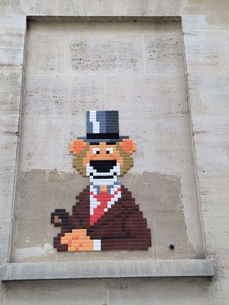 street art tile graffiti of a lion wearing a tuxedo and top hat. the mural is on a blank wall in paris with a niche so the mural looks framed.