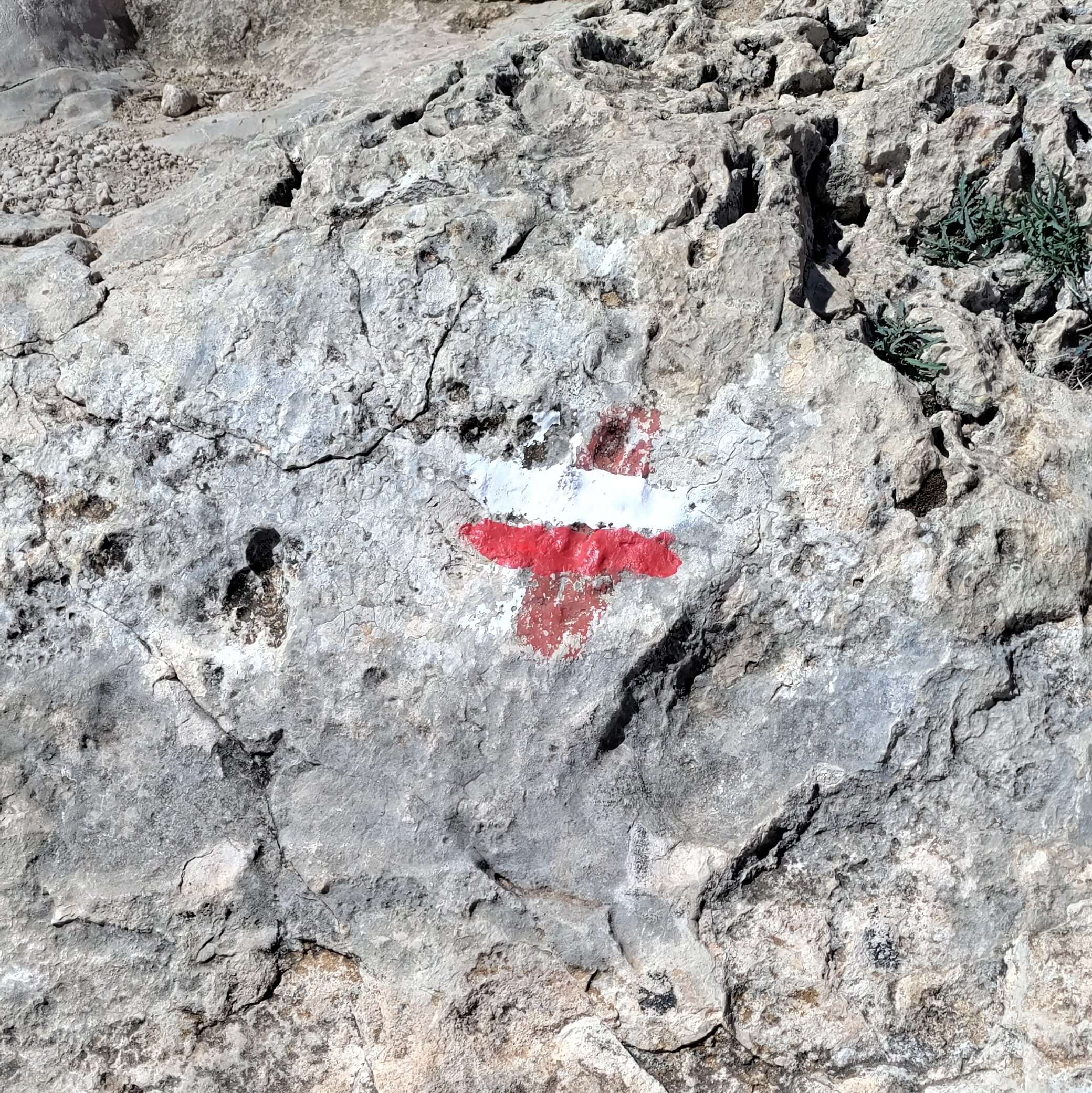 A blaze or trail marking painted on a rock. This blaze is horizontal stripes of white with red below reminiscent of a polish flag. It marks the trail to Playa del Muerto south of Sitges